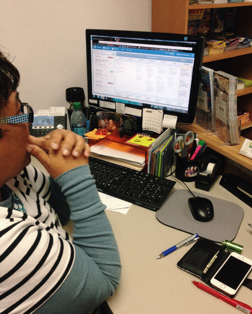 A woman sitting at her desk looking at a computer running FareHarbor